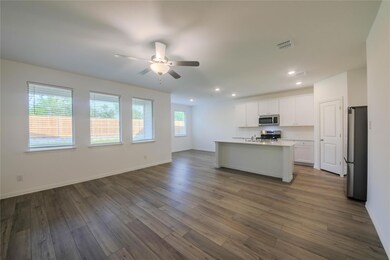 Kitchen with ceiling fan, stainless steel appliances, a center island with sink, wood-type flooring, and white cabinetry