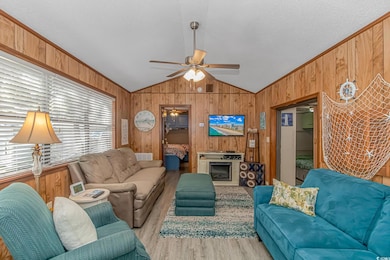 Living room with light wood-type flooring, lofted ceiling, ceiling fan, and wooden walls