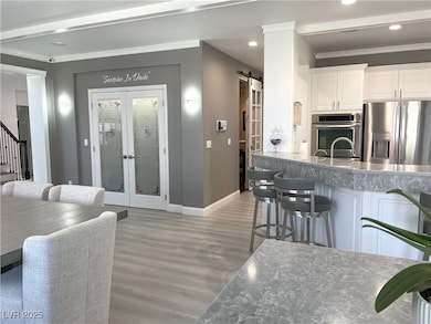 Kitchen with crown molding, french doors, stainless steel appliances, light wood-style flooring, and white cabinets
