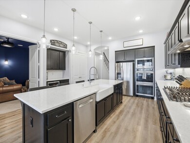 Kitchen with light stone countertops, light wood-style flooring, stainless steel appliances, pendant lighting, and a center island with sink