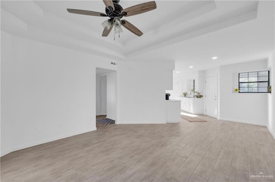 Unfurnished living room featuring a raised ceiling, light wood-style flooring, ceiling fan, and recessed lighting