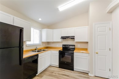 Kitchen featuring black appliances, lofted ceiling, light countertops, light wood finished floors, and white cabinetry