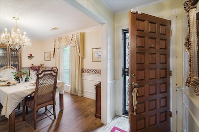 Entryway featuring a chandelier, wainscoting, light wood finished floors, crown molding, and a decorative wall