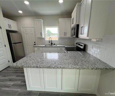 Kitchen with stainless steel appliances, a sink, a peninsula, light stone counters, and recessed lighting