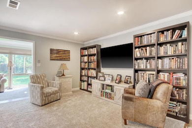 Living area featuring wall of books, carpet flooring, ornamental molding, recessed lighting, and baseboards