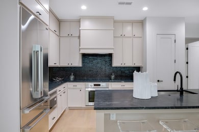 Kitchen with stainless steel appliances, decorative backsplash, a sink, light wood-style floors, and visible vents
