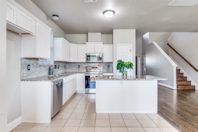 Kitchen featuring stainless steel appliances, white cabinetry, tasteful backsplash, light tile patterned floors, and light stone countertops
