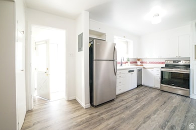 Kitchen with stainless steel appliances, decorative backsplash, white cabinets, light countertops, and light wood-style flooring