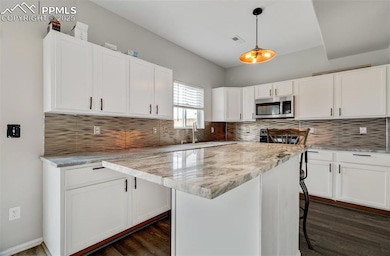 Kitchen with tasteful backsplash, white cabinetry, and pendant lighting