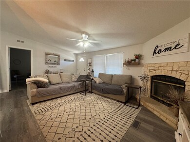 Living area featuring a textured ceiling, dark wood finished floors, a stone fireplace, and ceiling fan