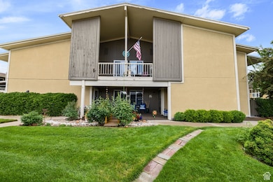 Rear view of property featuring a lawn, stucco siding, and a balcony