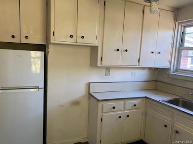 Kitchen featuring freestanding refrigerator, light countertops, white cabinets, and cream cabinetry