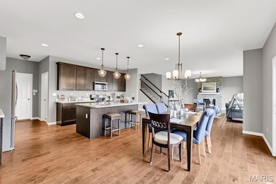 Dining room with light wood-type flooring, a stone fireplace, recessed lighting, a chandelier, and stairway