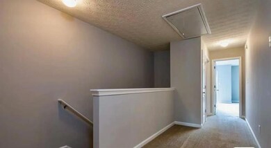 Corridor featuring attic access, an upstairs landing, a textured ceiling, carpet, and baseboards