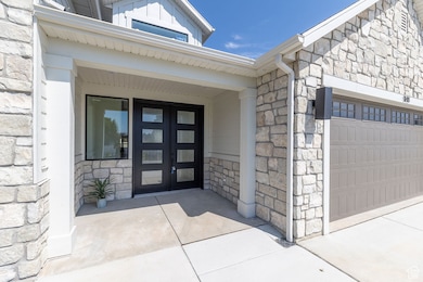 Property entrance featuring stone siding, french doors, a garage, and concrete driveway