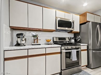 Kitchen featuring white cabinets, stainless steel appliances, light countertops, brown cabinets, and decorative backsplash
