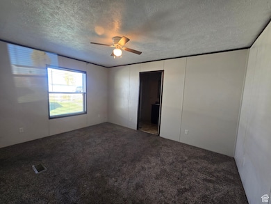 Unfurnished bedroom with dark colored carpet, a ceiling fan, a textured ceiling, and a decorative wall