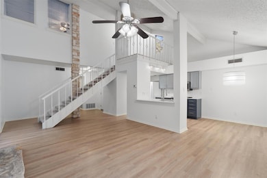 Unfurnished living room with a ceiling fan, beam ceiling, high vaulted ceiling, light wood-type flooring, and a textured ceiling