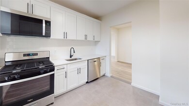 Kitchen with stainless steel appliances, white cabinets, light stone counters, backsplash, and light tile patterned flooring