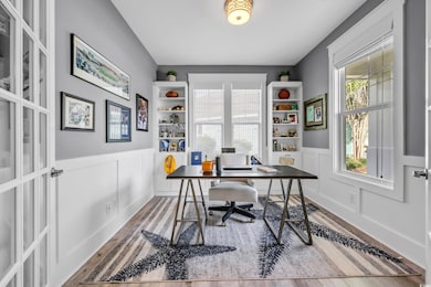 Office with wood finished floors, plenty of natural light, a wainscoted wall, and a decorative wall