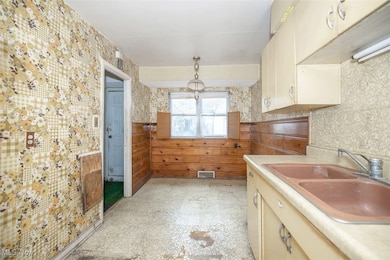 Kitchen featuring light flooring, light countertops, wallpapered walls, cream cabinets, and hanging light fixtures