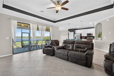 Living area with crown molding, light tile patterned floors, ceiling fan, a water view, and a tray ceiling