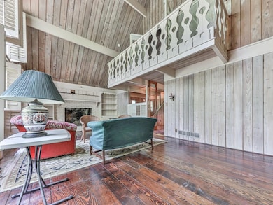 Living room featuring hardwood / wood-style flooring, a brick fireplace, wooden walls, and beamed ceiling