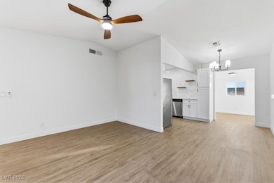 Living room with vaulted ceiling, light wood-type flooring, ceiling fan, and a chandelier