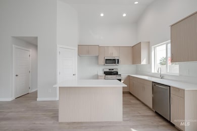Kitchen featuring a towering ceiling, light brown cabinetry, a kitchen island, appliances with stainless steel finishes, and light wood-style floors