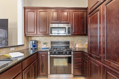 Kitchen featuring stainless steel appliances, dark granite counters, rich brown cabinets, decorative backsplash, and open to living.