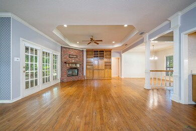 Unfurnished living room featuring a fireplace, a raised ceiling, wood finished floors, ceiling fan, and a chandelier