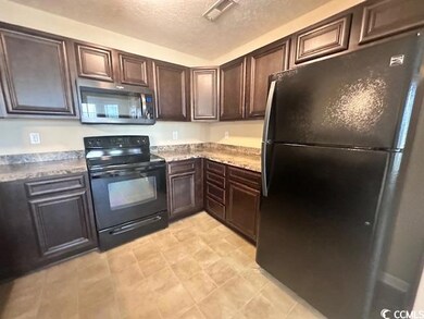 Kitchen with black appliances, a textured ceiling, dark brown cabinetry, and light stone counters