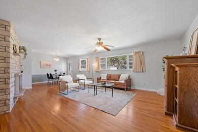 Living area with light wood finished floors, a stone fireplace, a chandelier, and a ceiling fan