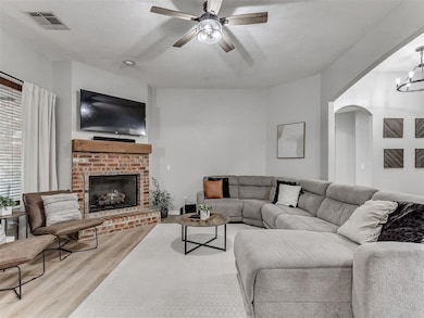 Living room with wood finished floors, a ceiling fan, a fireplace, arched walkways, and a chandelier