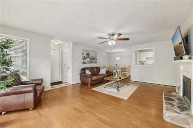 Living area with ceiling fan, wood finished floors, a fireplace with raised hearth, and baseboards