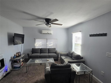 Carpeted living room with a ceiling fan, a textured ceiling, a textured wall, and heating unit