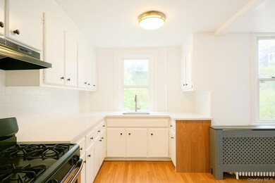 Kitchen featuring gas stove, radiator heating unit, light countertops, and white cabinetry