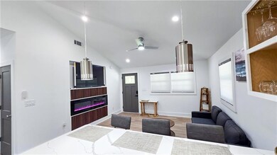 Living area featuring a glass covered fireplace, plenty of natural light, a ceiling fan, wood finished floors, and high vaulted ceiling
