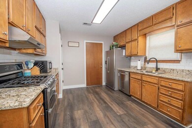 Kitchen with appliances with stainless steel finishes, under cabinet range hood, dark wood-style flooring, backsplash, and brown cabinetry