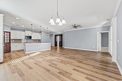 Unfurnished living room with a chandelier, crown molding, light wood-type flooring, ceiling fan, and recessed lighting.