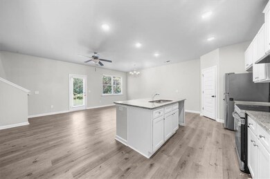 Kitchen featuring stainless steel electric stove, a sink, ceiling fan, a center island with sink, and white cabinetry