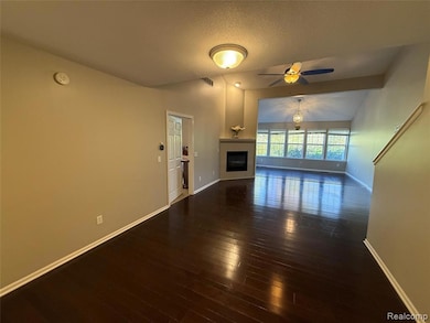 Unfurnished living room with a glass covered fireplace, dark wood finished floors, vaulted ceiling, a textured ceiling, and a ceiling fan