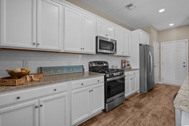 Kitchen featuring appliances with stainless steel finishes, white cabinetry, wood finished floors, light stone countertops, and backsplash