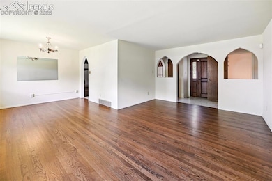 Unfurnished living room with a chandelier, wood finished floors, and arched walkways