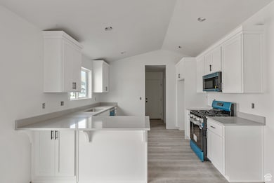 Kitchen featuring a breakfast bar, stainless steel gas range oven, lofted ceiling, white cabinets, and a peninsula
