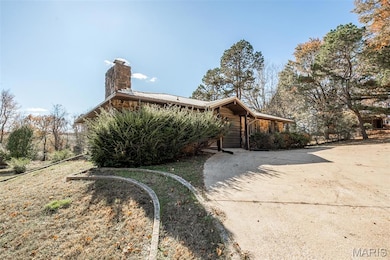 View of home's exterior featuring a chimney, a metal roof, and driveway