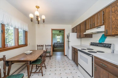 Kitchen with under cabinet range hood, white appliances, light flooring, light countertops, and a chandelier