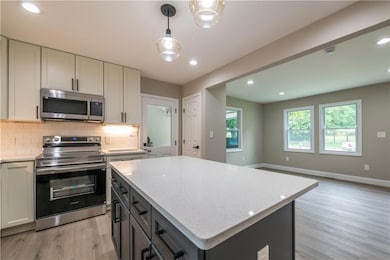Kitchen with stainless steel appliances, light wood-style floors, tasteful backsplash, a kitchen island, and light stone countertops