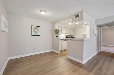 Open kitchen with white cabinets, light countertops, a textured ceiling, light wood-type flooring, and bar