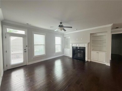 Unfurnished living room with ceiling fan, ornamental molding, built in shelves, dark wood finished floors, and a glass covered fireplace